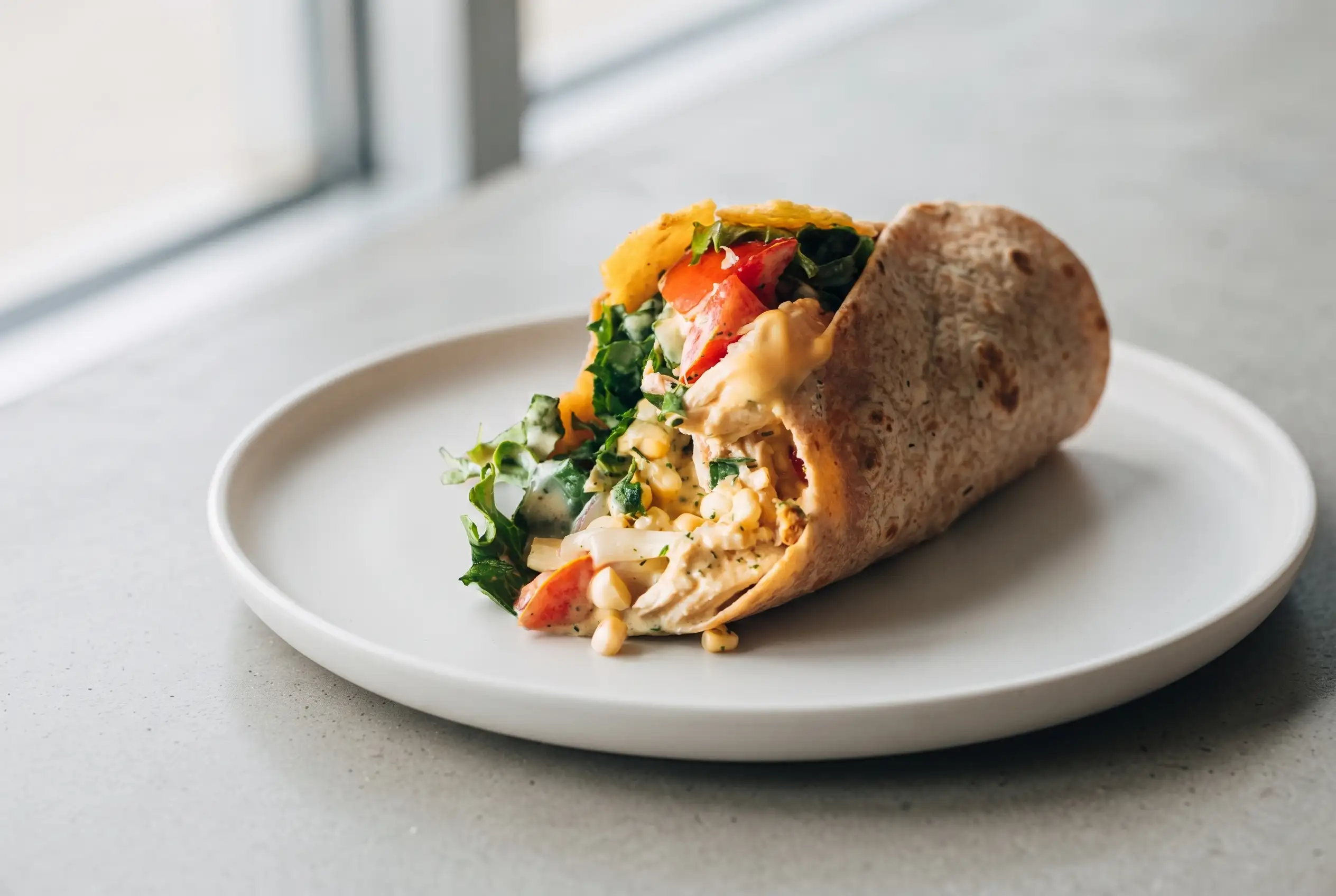 Chicken wraps with grilled chicken, cheddar crisp, lettuce, tomato, corn, and sauces in a whole wheat tortilla