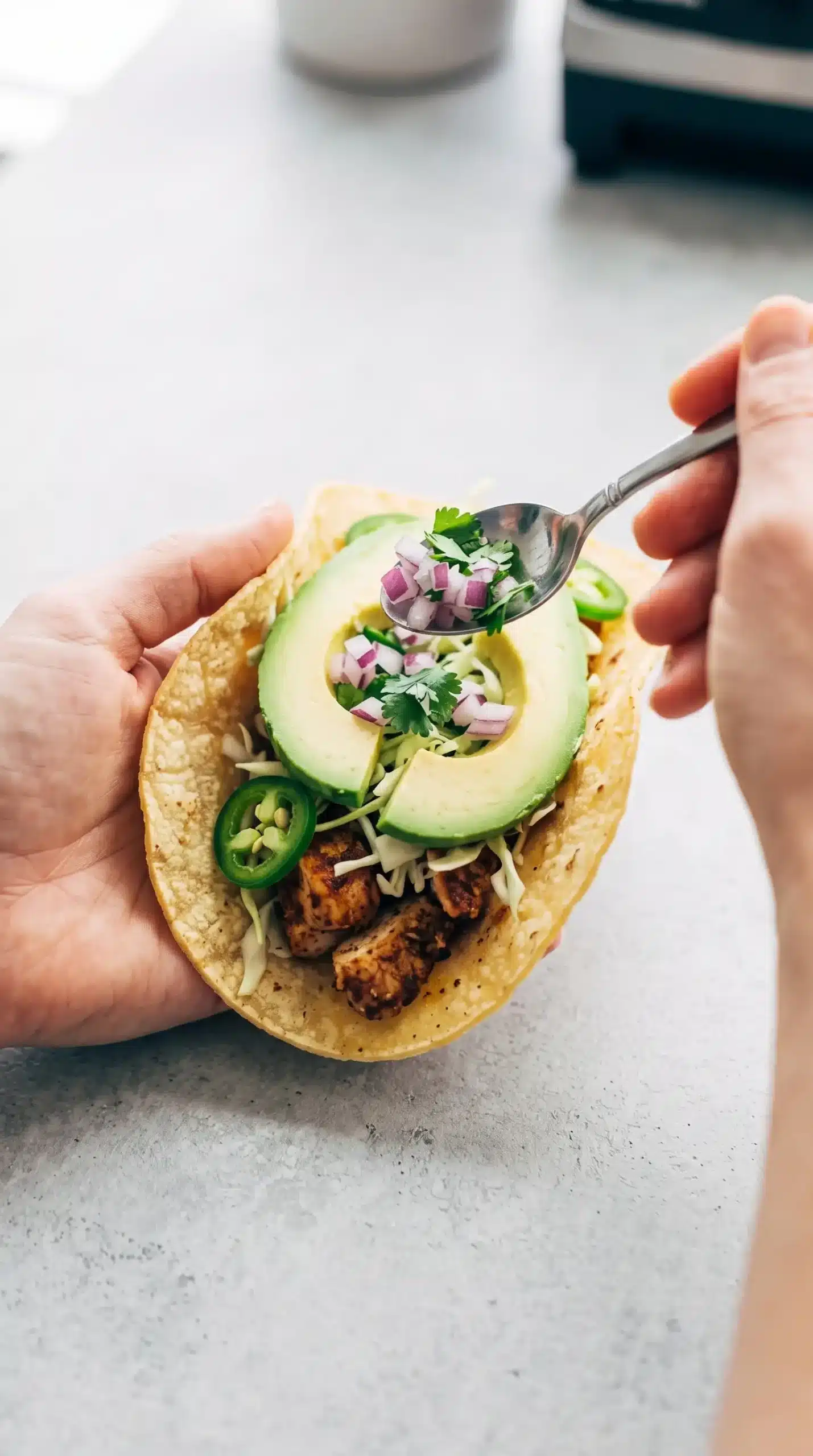 Warm corn tortilla being filled with ancho chicken and fresh taco toppings