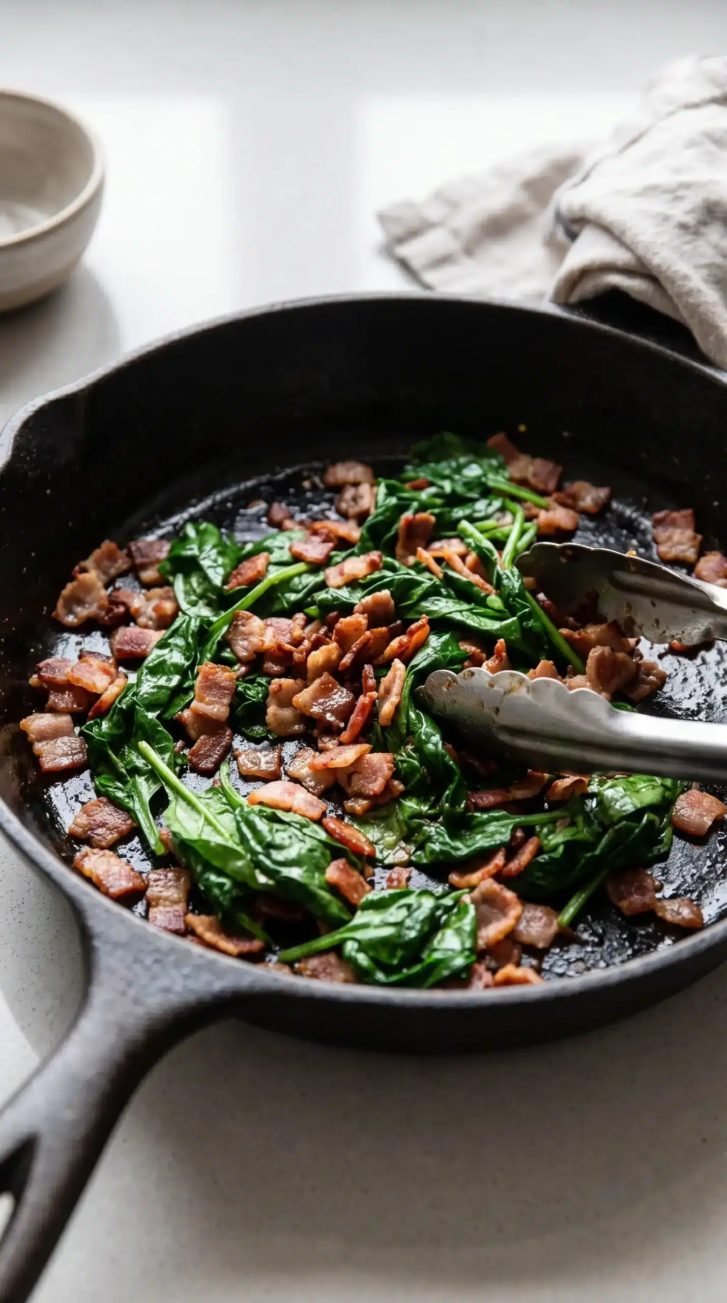 Cooked bacon pieces and spinach mixture prepared for breakfast sandwich filling