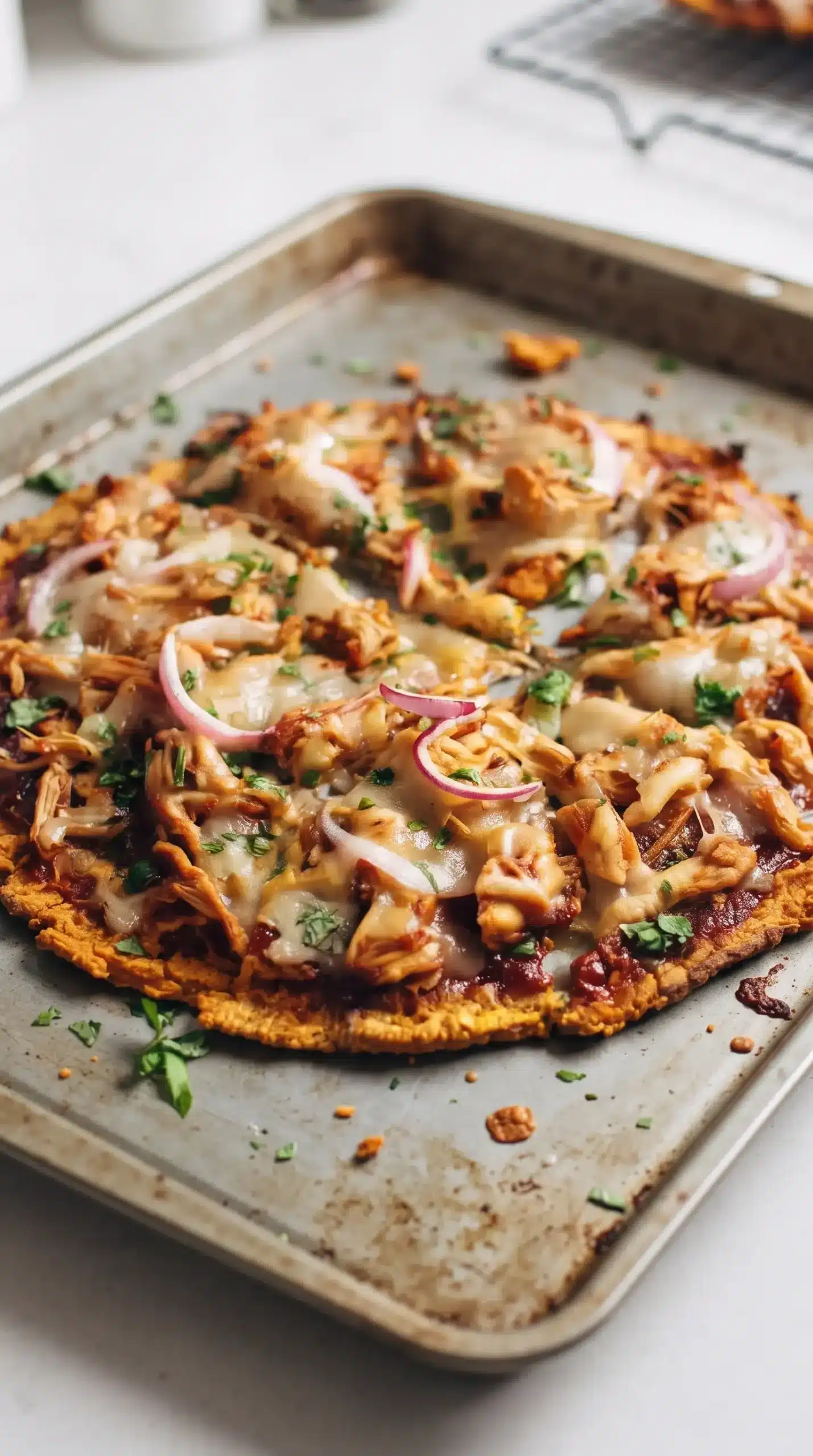 Baked BBQ chicken pizza on a tray with melted mozzarella and sweet potato crust edges