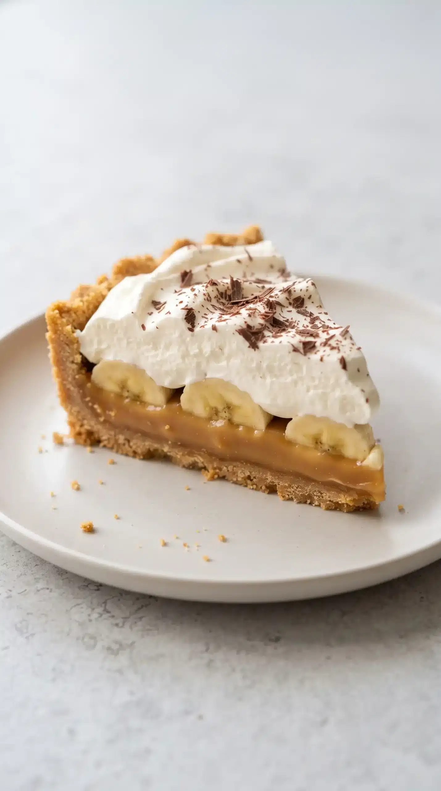 Banoffee pie slice showing graham crust, toffee, banana, cream, and chocolate layers