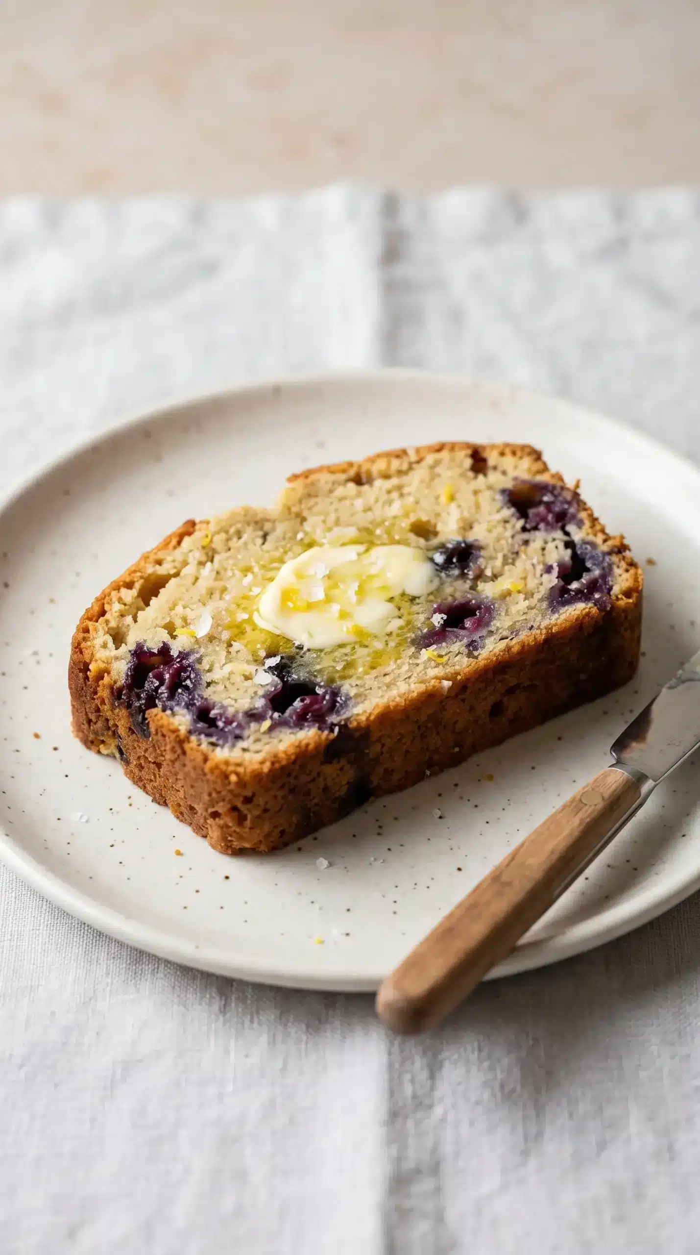 Slice of blueberry lemon loaf with butter showing a tender berry-filled crumb