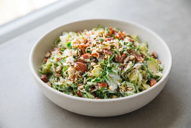 Brussels sprout salad with bacon, citrus dressing, almonds, and Parmesan in a ceramic bowl