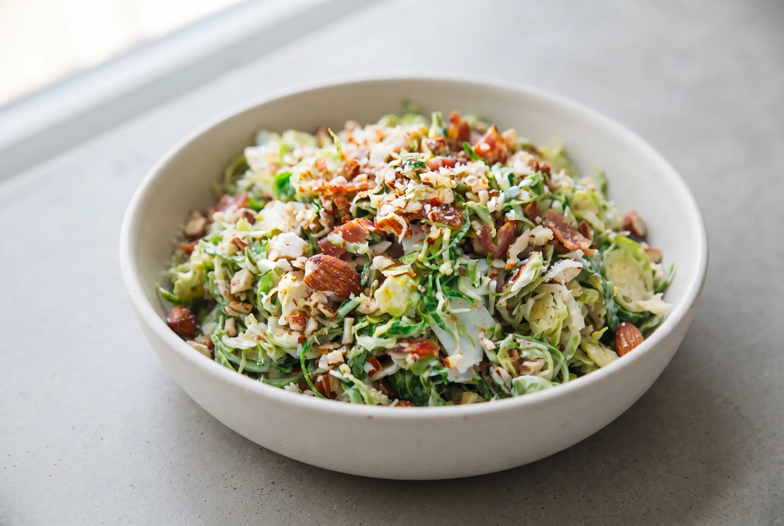 Brussels sprout salad with bacon, citrus dressing, almonds, and Parmesan in a ceramic bowl