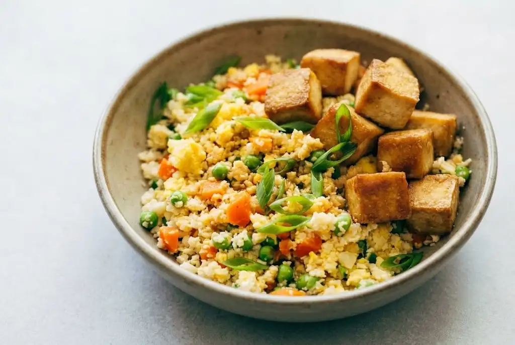 Cauliflower Fried Rice with Crispy Tofu Cauliflower fried rice with crispy tofu, scrambled eggs, vegetables, and green onions in a bowl