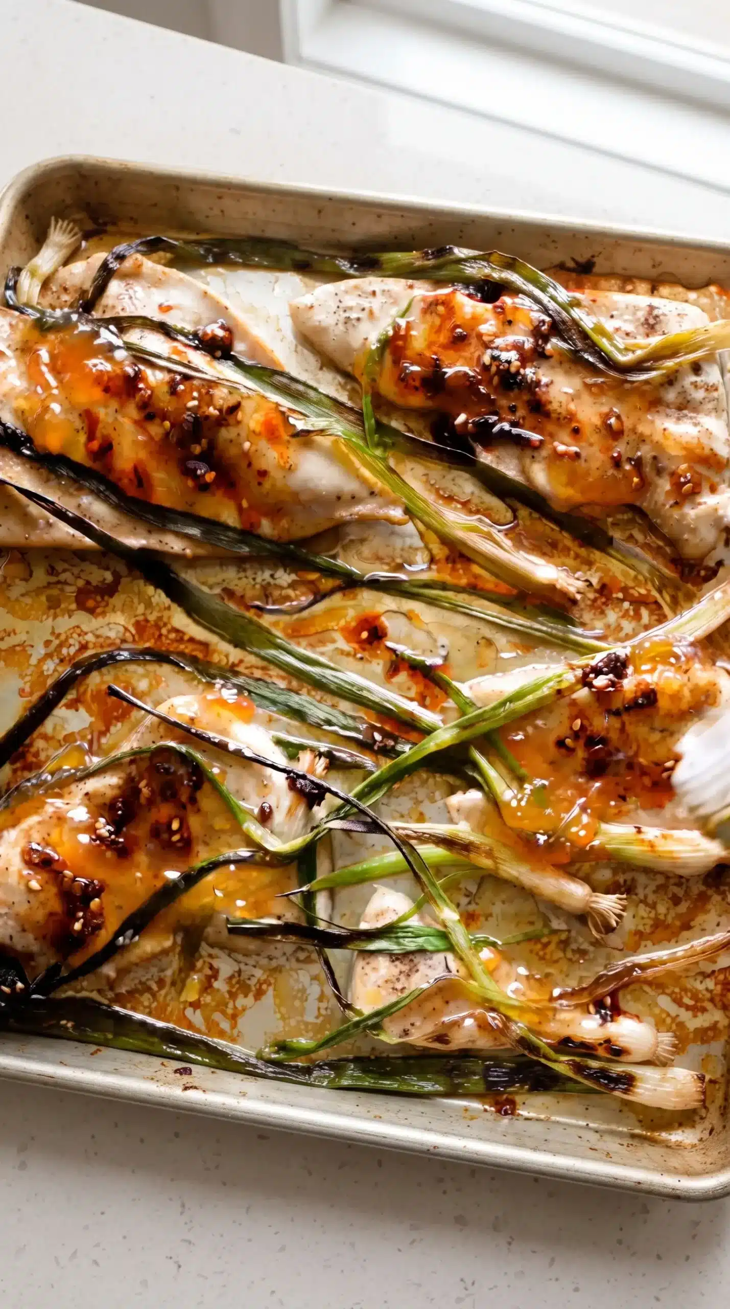 Baked sesame apricot chicken topped with browned charred scallions on a sheet pan