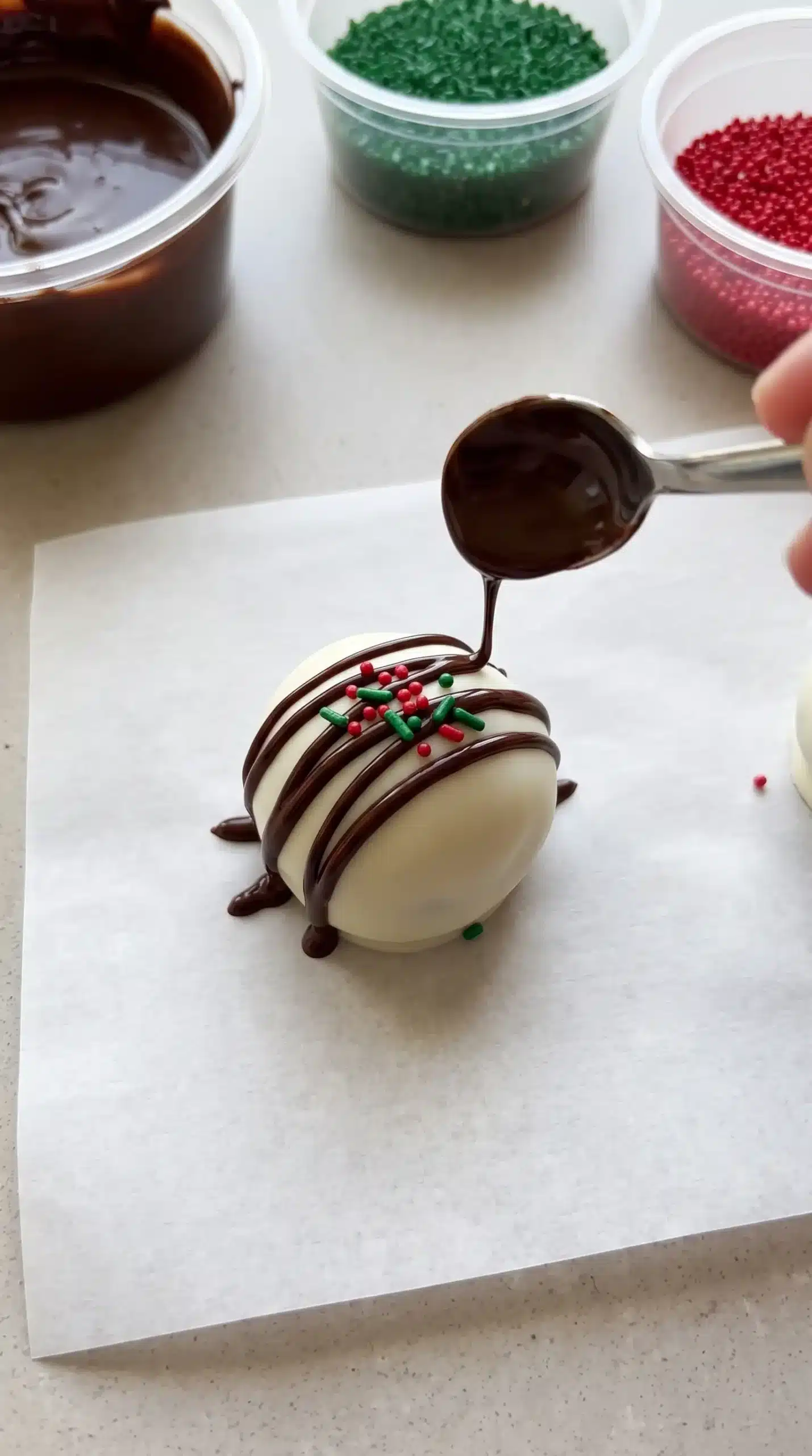 Coated chocolate cake bite being topped with chocolate drizzle and holiday sprinkles