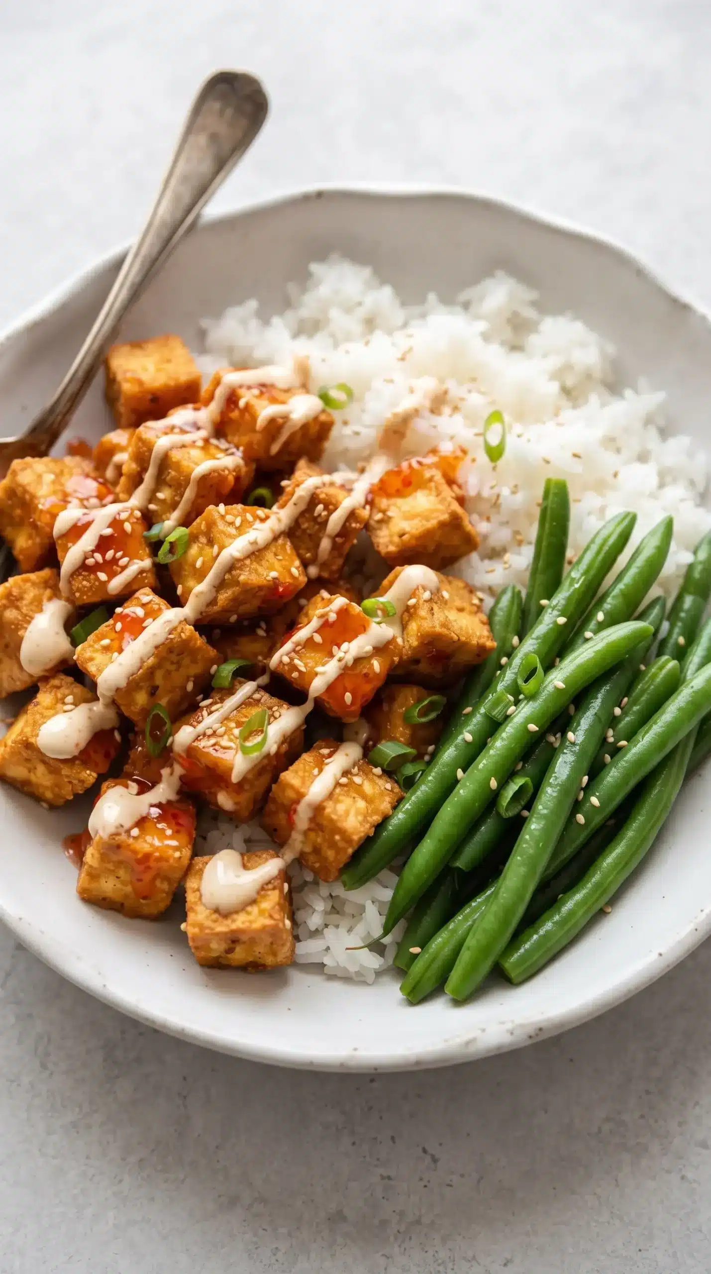 Bang bang tofu bowl with creamy sauce, rice, green beans, sesame seeds, and green onions
