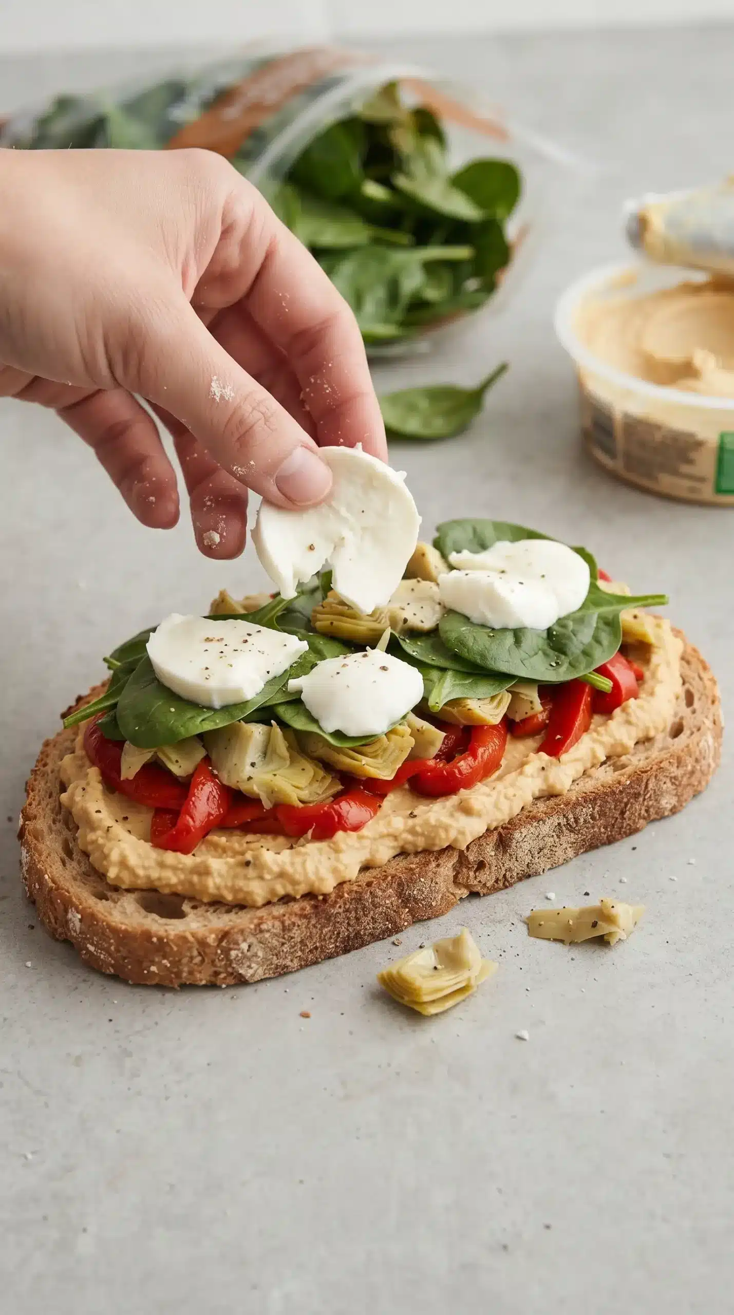 Layering roasted red peppers, artichokes, spinach, and mozzarella on a hummus-covered melt