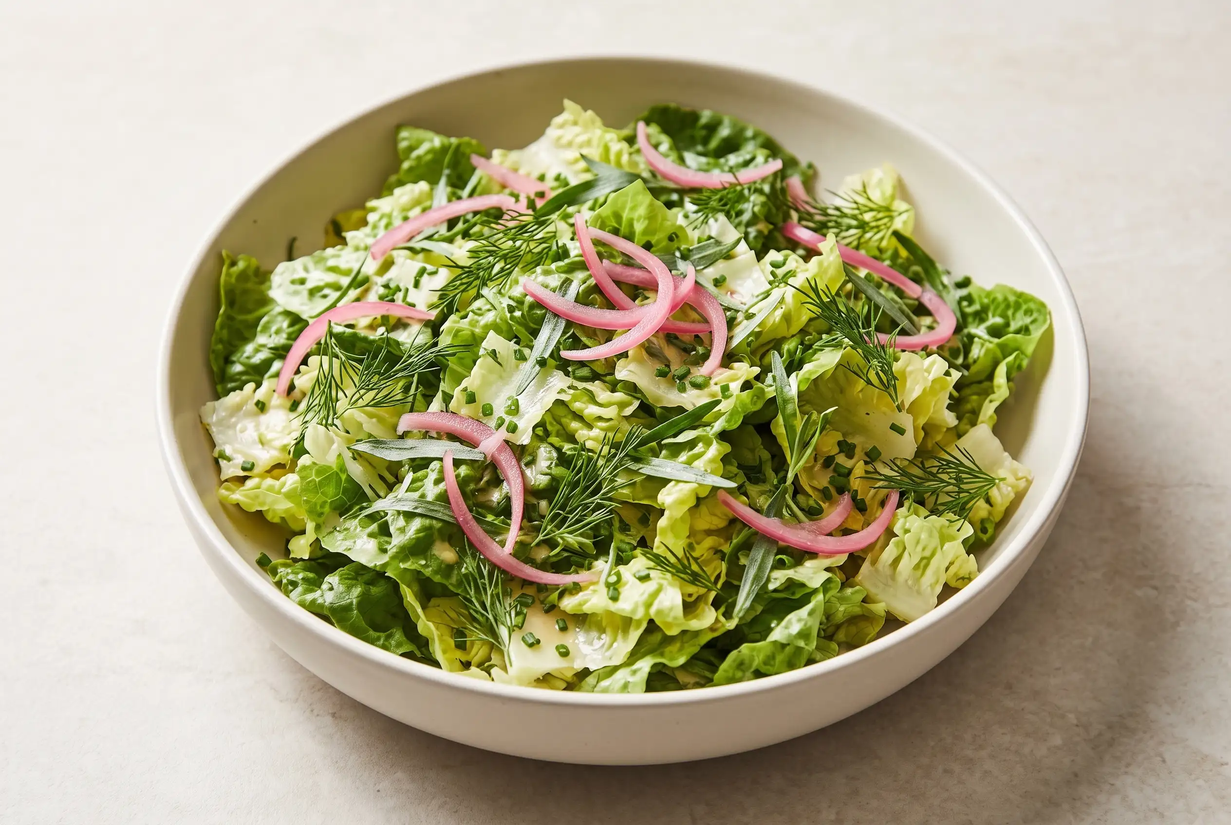 Bistro salad with crisp lettuce, fresh herbs, and pink pickled onions in a ceramic bowl