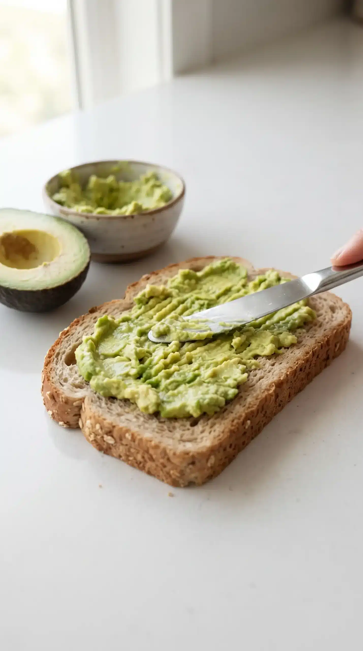 Mashed avocado spread onto wheat bread during avocado veggie panini assembly