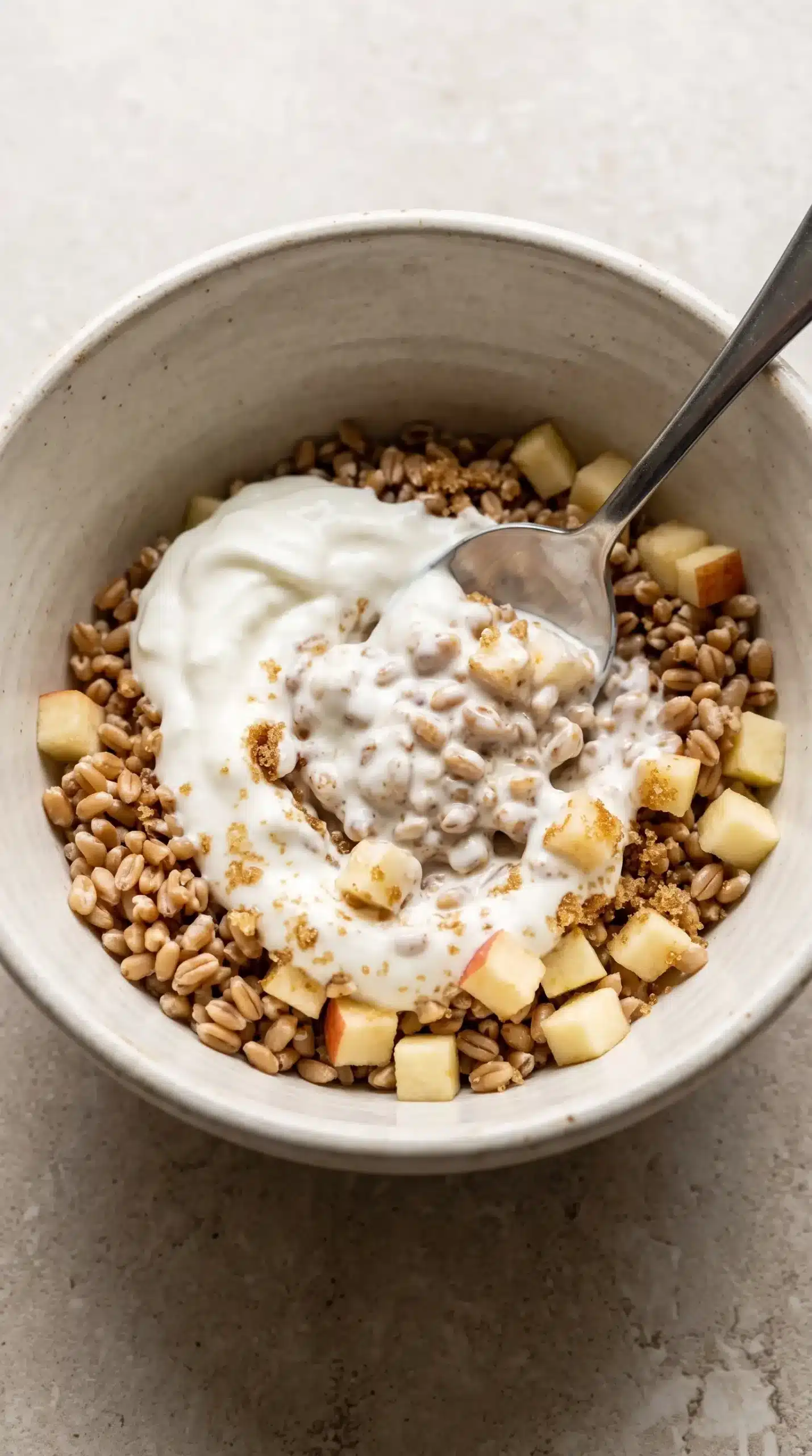 Greek yogurt mixed with cooked wheat berries and diced apples in a bowl during parfait preparation