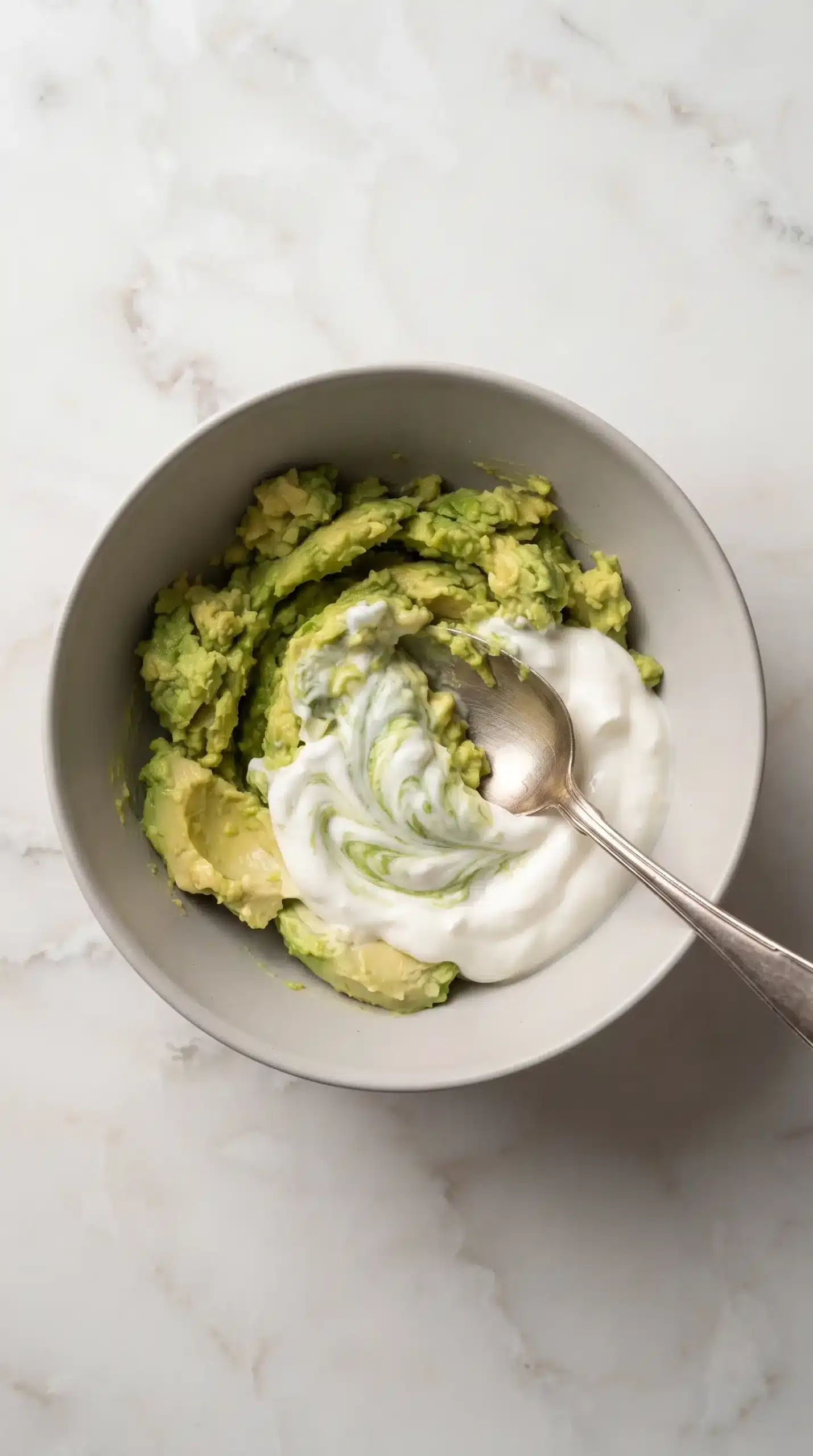 Mashed avocado being mixed with Greek yogurt for a creamy dip