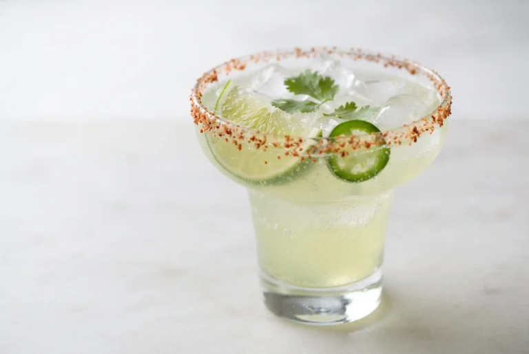 Non alcoholic margarita with lime drink, Tajin rim, ice, lime wedge, cilantro, and jalapeño garnish