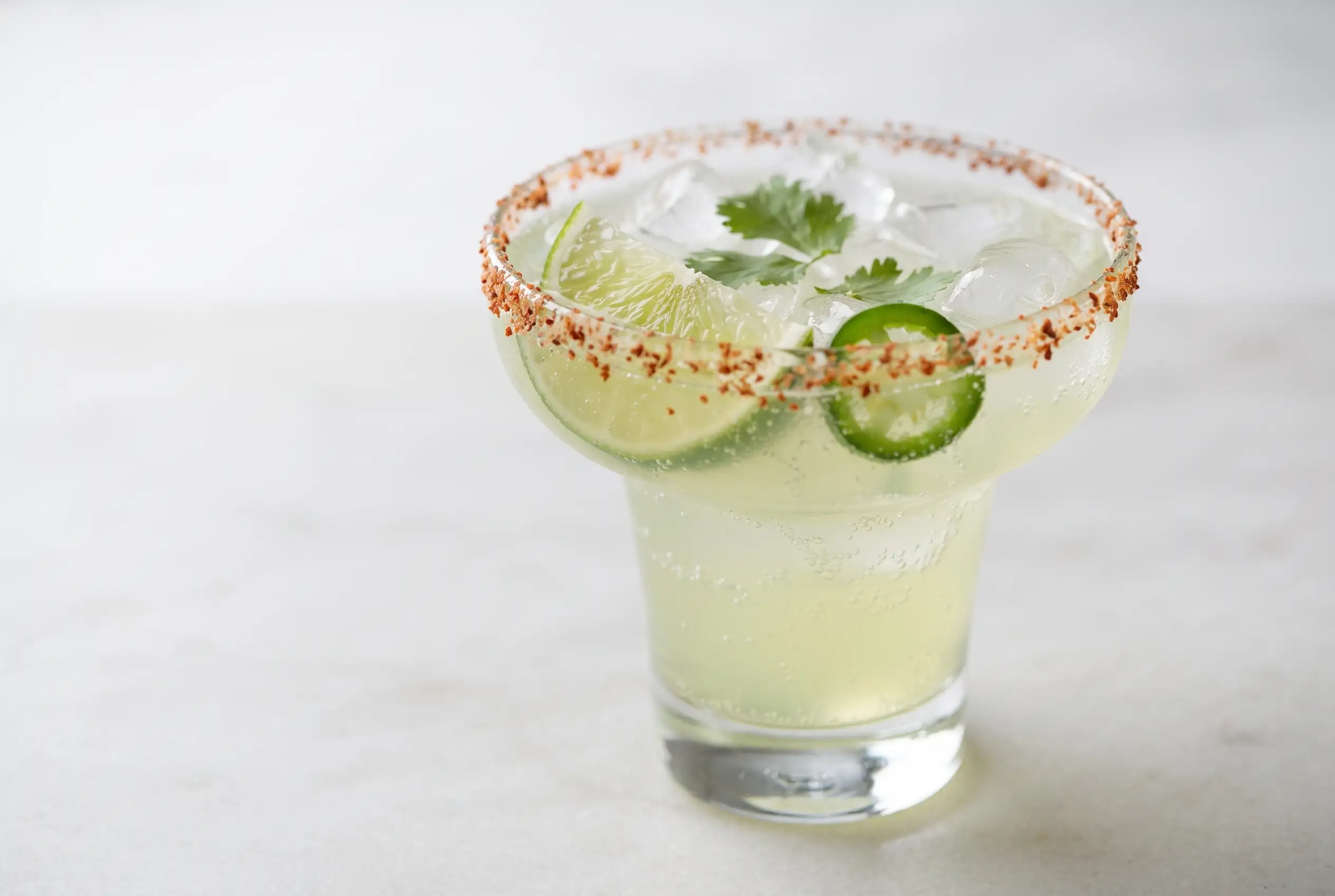 Non alcoholic margarita with lime drink, Tajin rim, ice, lime wedge, cilantro, and jalapeño garnish