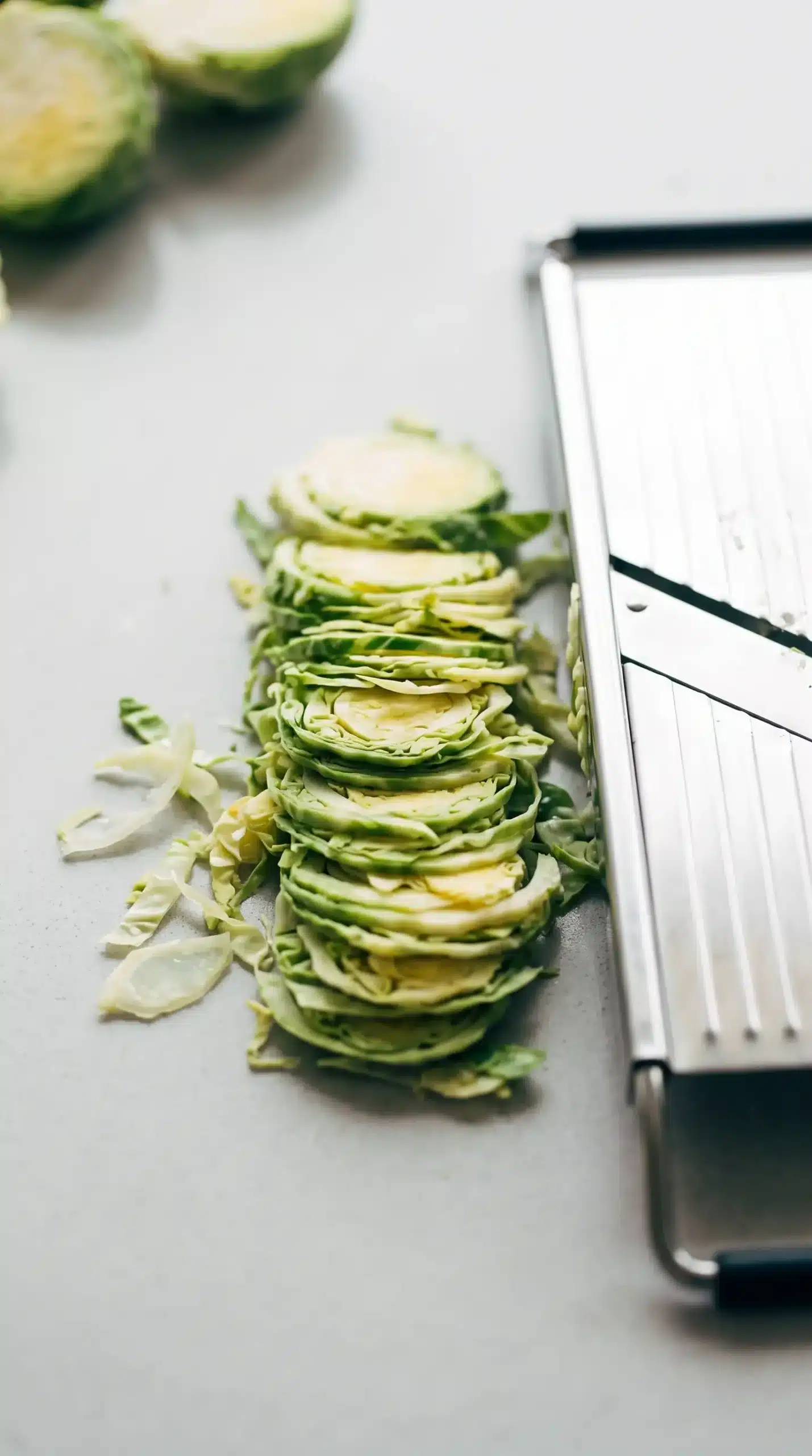 Thinly shredded Brussels sprouts beside a mandoline for salad preparation