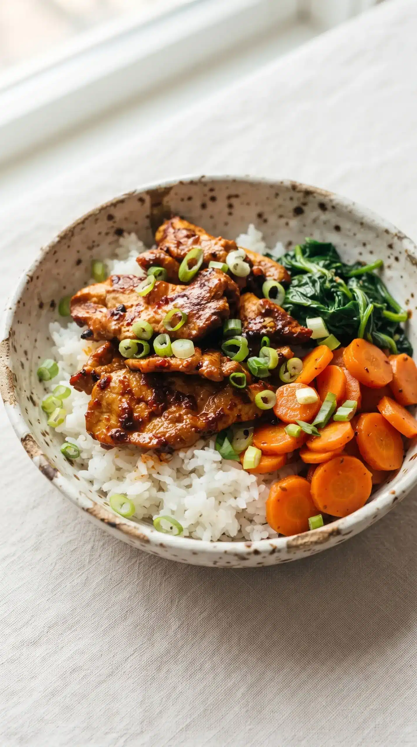 Spicy pork bowl with caramelized pork, white rice, spinach, carrots, and green onions